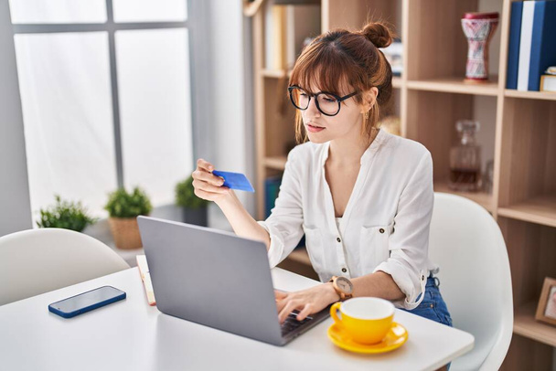 Молода жінка, використовуючи ноутбук і кредитну картку, сидить на столі вдома
 - Фото, зображення