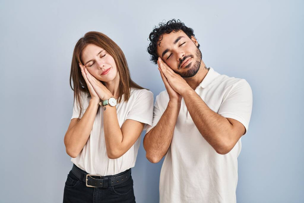 Young couple wearing casual clothes standing together sleeping tired dreaming and posing with hands together while smiling with closed eyes.  - Foto, afbeelding