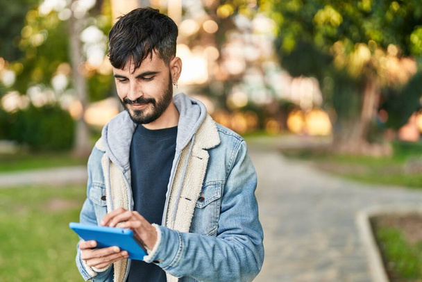 Νεαρός Ισπανόφωνος χαμογελά σίγουρος χρησιμοποιώντας touchpad στο πάρκο - Φωτογραφία, εικόνα