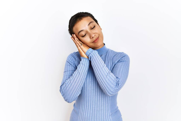 Young hispanic woman with short hair standing over isolated background sleeping tired dreaming and posing with hands together while smiling with closed eyes.  - Foto, afbeelding