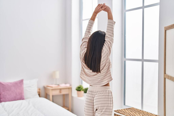 Mujer hispana joven estirando brazos de pie en el dormitorio - Foto, imagen
