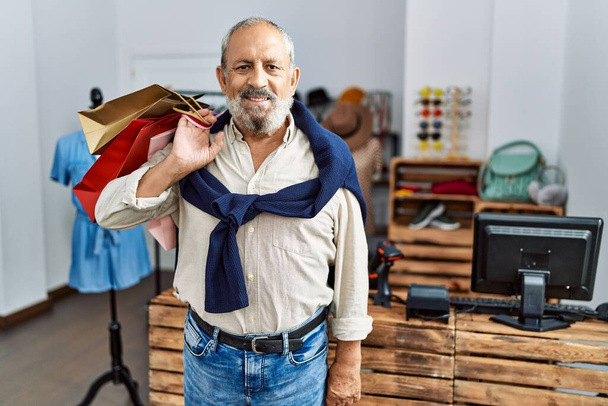 Старший седой мужчина улыбается уверенно держа сумки в магазине одежды - Фото, изображение