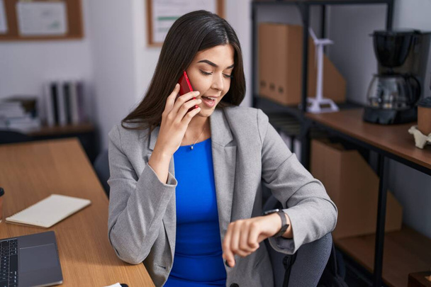 Fiatal gyönyörű spanyol nő üzleti dolgozó beszél okostelefonon keres óra irodában - Fotó, kép