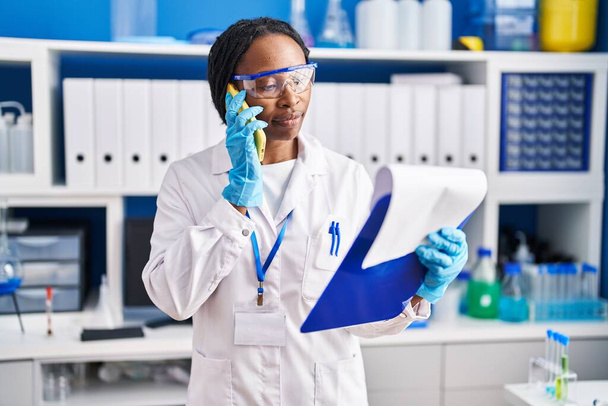 Africano mulher americana vestindo uniforme cientista falando no laboratório de smartphones - Foto, Imagem
