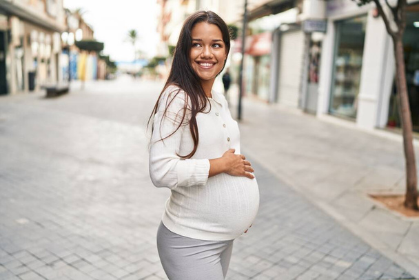 Mladý latina žena těhotná usměvavý jistý dojemný břicho na ulici - Fotografie, Obrázek