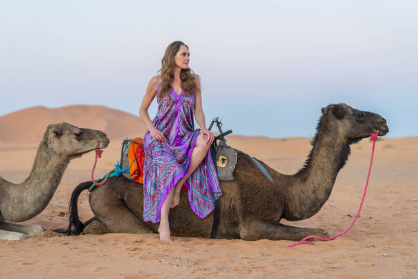 Piękny model jeździ na wielbłądzie po Saharyjskiej Pustyni w Maroku - Zdjęcie, obraz