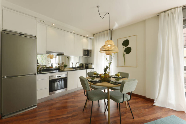 Salón con cocina abierta, con mesa de comedor con mesa redonda de madera y sillas tapizadas en tela verde - Foto, imagen