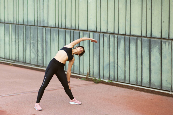 Full length portrait of young woman doing stretching exercise outside in the city - Photo, Image