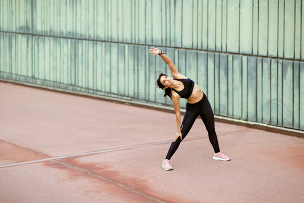 Full length portrait of healthy young woman doing sideways body stretching exercise outside - Fotoğraf, Görsel