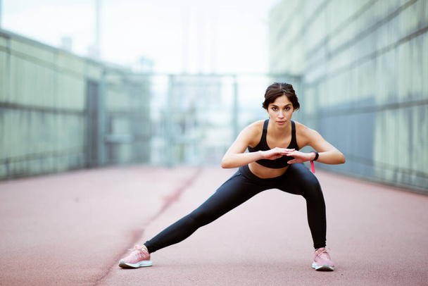 Ganzkörperporträt einer aktiven Frau, die morgens draußen ihre Muskeln dehnt - Foto, Bild