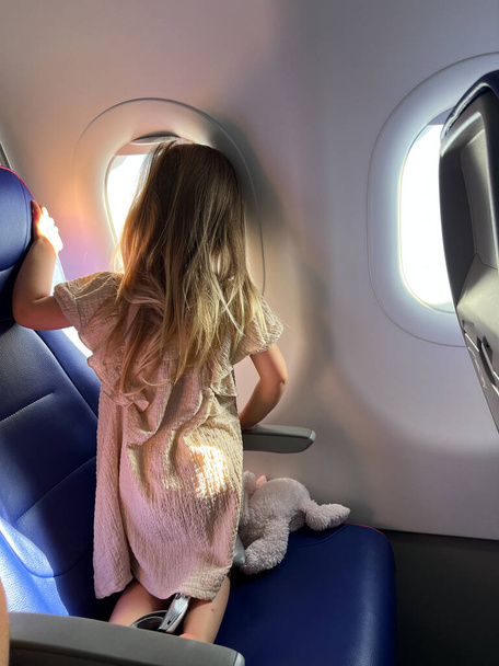 Little girl kneels on the seat and looks out the window. Back view. High quality photo - Photo, Image