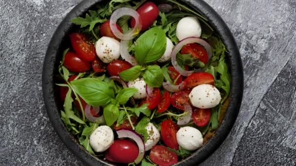Salad with traditional italian mozzarella cheese with arugula and tomatoes on dark concrete table with cooking ingredients cherry tomatoes, basil. Top view. - Filmagem, Vídeo