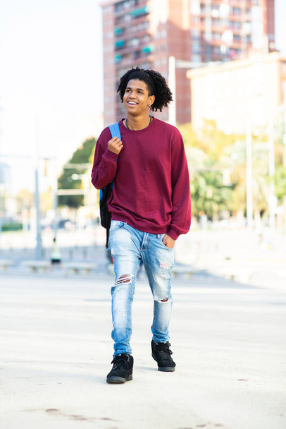 Hombre afroamericano feliz caminando al aire libre con mochila en la ciudad - Foto, imagen