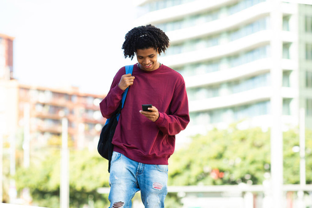 Happy african american man text messaging using mobile phone outdoors in city - Photo, Image