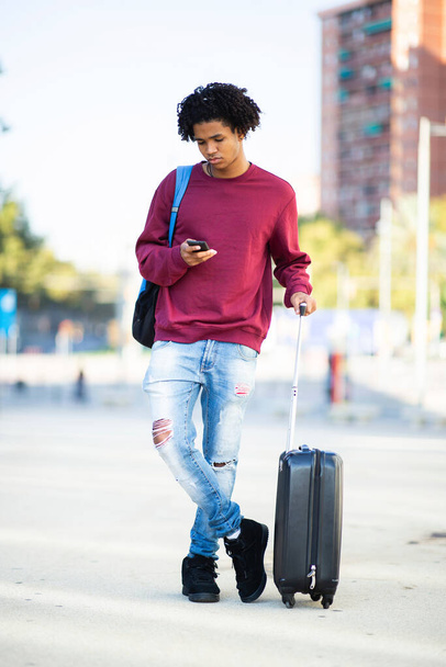 African american man with luggage messaging using mobile phone outdoors in city - Zdjęcie, obraz