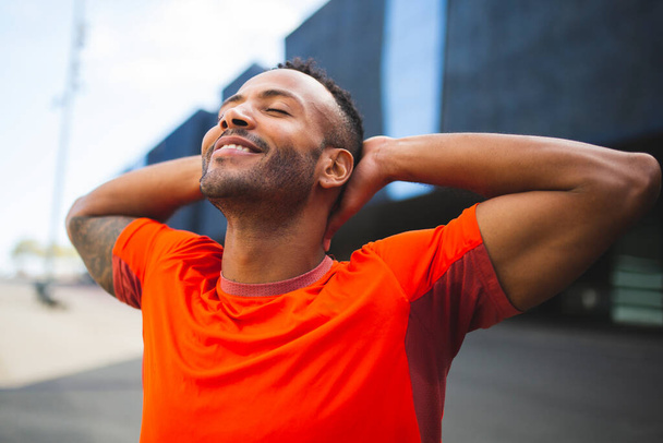 Щасливий чоловік у спортивному одязі, що розтягується на відкритому повітрі своїми руками за голову
 - Фото, зображення