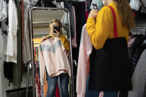 Shopping, Mode, Stil und People-Konzept - glückliche Frau, die Kleidung auswählt und sich in Einkaufszentrum oder Bekleidungsgeschäft spiegelt - Foto, Bild