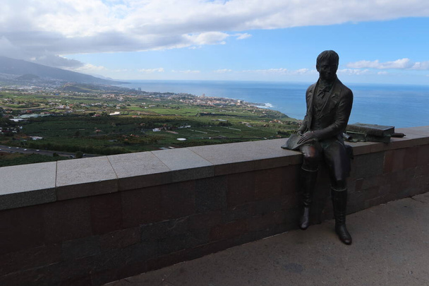 La Orotava, Tenerife, Spain, February 23, 2022: Sculpture of the German naturalist Alexander Von Humboldt at the Humboldt viewpoint with the Atlantic Ocean and Puerto de la Cruz in the background. La Orotava, Tenerife. Spain - Foto, imagen