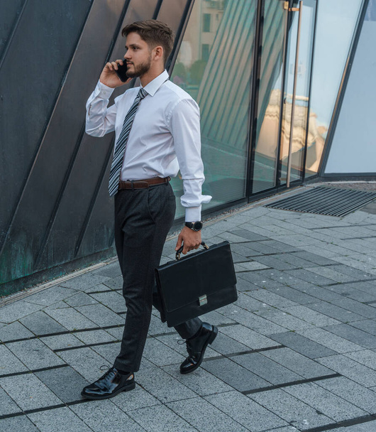 Портрет серьезного бизнесмена, одетого в формальную одежду, разговаривающего по телефону на улице. - Фото, изображение
