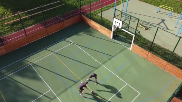 Two friends play one-on-one basketball on an artificial court in summer weather. Active leisure time. Relieve stress by playing. 4k video - Materiał filmowy, wideo