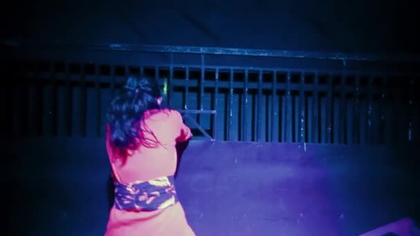 Heartbroken Asian Women dancing in front of the black fence with purple lighting in the dark night - Felvétel, videó