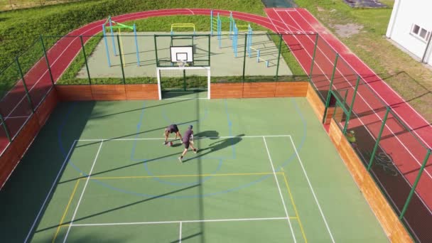 Two friends play one-on-one basketball on an artificial court in summer weather. Active leisure time. Relieve stress by playing. 4k video - Materiał filmowy, wideo