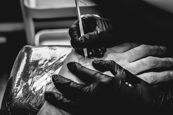 Detalhe das mãos do tatuador com luvas pretas fazendo uma nova tatuagem com tonalidade branca de yin yang na mão de um cara com a técnica tradicional japonesa de 'mão picada' (em preto e branco) - Foto, Imagem