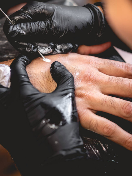 Деталь рук татуировщика в черных перчатках, делающего новую татуировку с белым оттенком инь-янь в руке парня с традиционной японской техникой "тычка в руку" - Фото, изображение
