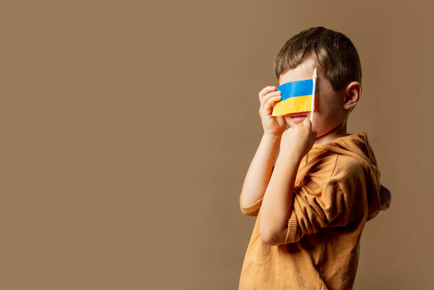 Little kid boy with Ukrainian flag on brown background - Fotoğraf, Görsel