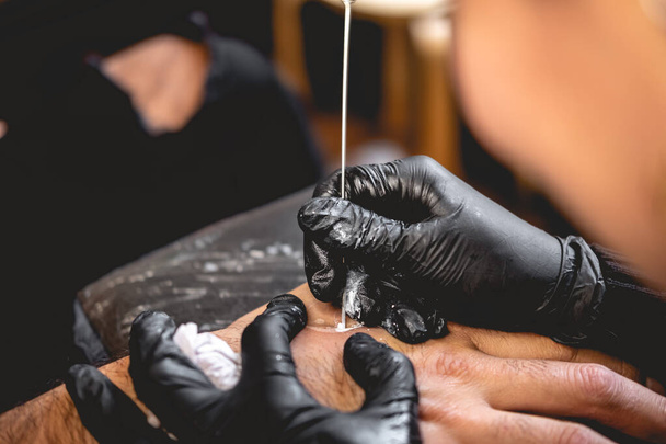 Detail van handen van tatoeëerder met zwarte handschoenen maken van een nieuwe tatoeage met witte tint van yin yang in de hand van een man met traditionele Japanse 'hand porren' techniek - Foto, afbeelding