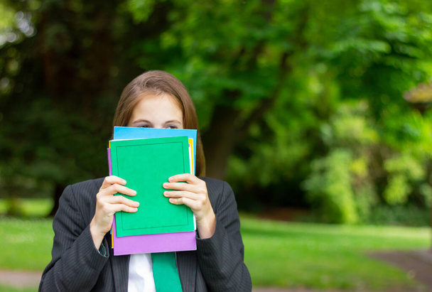 portrait of a teenage school girl in a uniform covers her face with a notebook, only her eyes are visible. - Photo, image