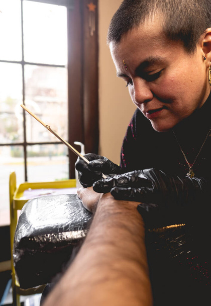 Joven artista del tatuaje chica con el pelo muy corto haciendo un nuevo tatuaje de yin yang en la mano de un chico con tradicional japonés 'mano poke' técnica - Foto, Imagen
