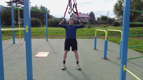 active, enthusiastic athlete performs exercises for a stronger midsection and stretching of the respective limbs on Trx fitness straps. Train upper body chest shoulders pecs triceps. - Materiał filmowy, wideo