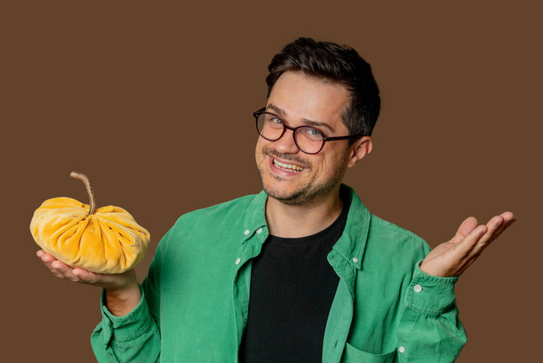 Stylish man in glasses and green shirt hold pumpkin in hand on brown background - Fotografie, Obrázek