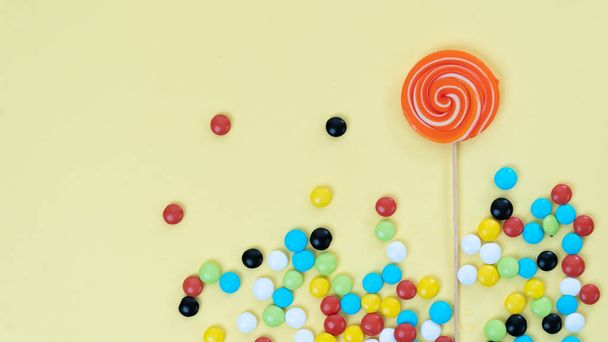 Sweets on a bright colored background - lollipop and multi-colored dragee with space for text. High quality photo - Photo, Image