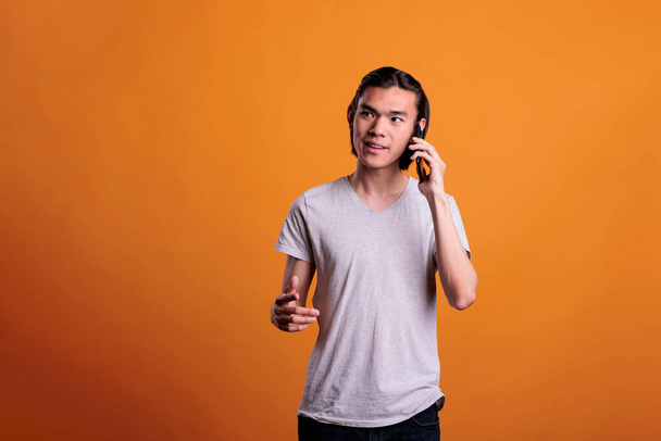 Young smiling man talking on smartphone. Asian teenager chatting on telephone, attractive person with positive facial expression having mobile conversation, answering phone call - Photo, Image