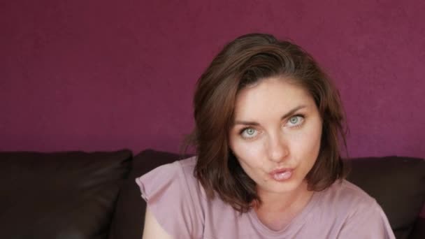 Close-up portrait of a young beautiful woman with green eyes and dark hair, who looks directly into the camera with tenderness and smiles, touches her face and hair, flirting, winking. - Materiaali, video