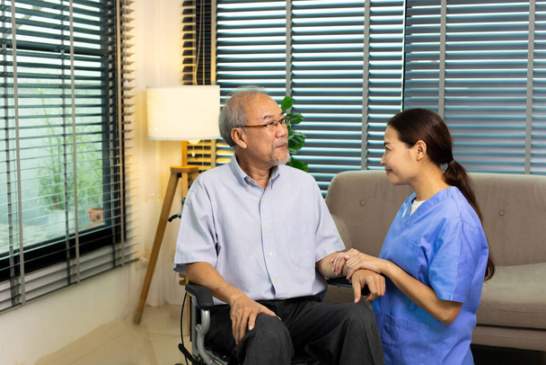 Asian Nurse take care Elderly Senior Man with warm welcome. 70s Mature Man patient has good health and support help by Caregiver from medical hospital. Grandfather sit on wheelchair, copy space - Foto, Bild