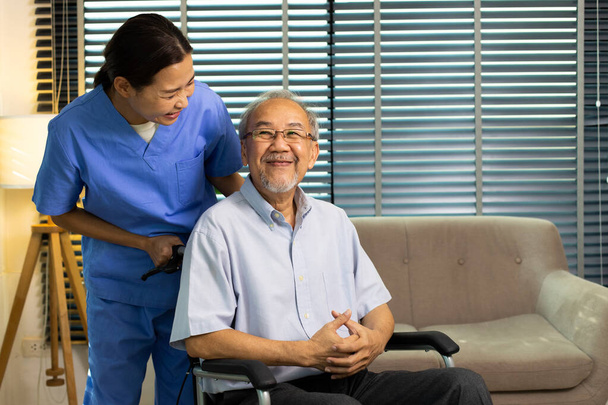 Asian Nurse take care Elderly Senior Man with warm welcome. 70s Mature Man patient has good health and support help by Caregiver from medical hospital. Grandfather sit on wheelchair, copy space - Photo, image