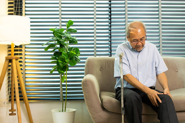 Grandfather unhappy health from pain Knee injury. Senior Elderly man has problem on joint knee leg and suffer ache health care problem when sitting and need walker staff to support help, copy space - 写真・画像