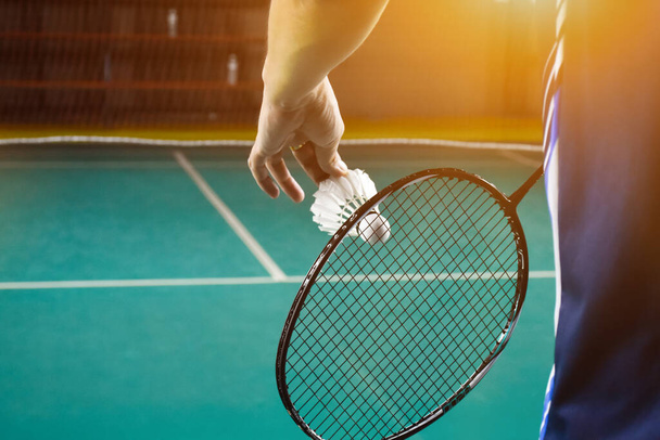 Badminton player holds racket and white cream shuttlecock in front of the net before serving it to another side of the court. - Foto, afbeelding