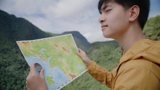 Teenager tourist hiking in forest looking at a map and using a compass, Mountains all around - Filmati, video