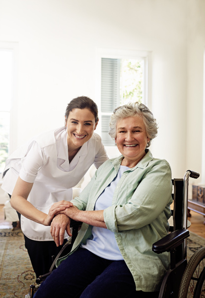 She always brings a smile to her patients. Portrait of a smiling caregiver and a senior woman in a wheelchair at home - Foto, Imagem