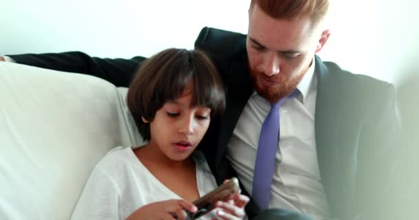 Candid Father and son together at home couch sharing cellphone screen. Mixed race ehtnically diverse parent and child - Video