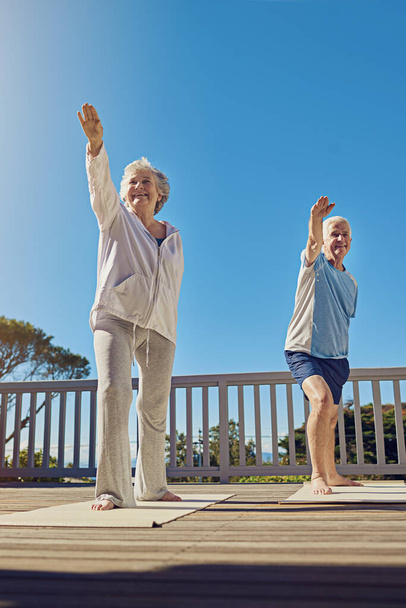 Улучшение здоровья в золотые годы. старшая пара, занимающаяся йогой вместе на террасе - Фото, изображение