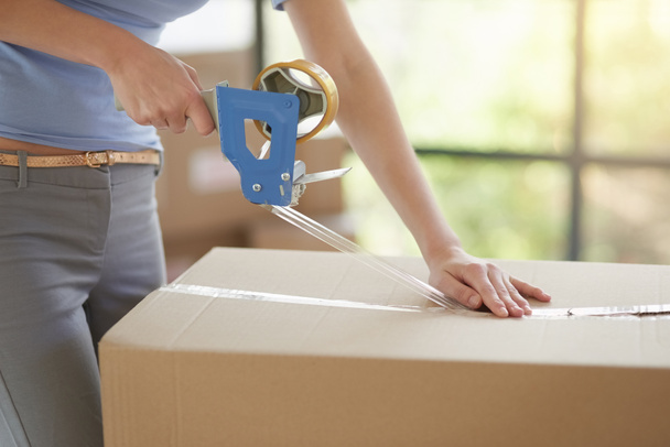Packing her possessions for the big move. an unidentifiable young woman closing a cardboard box with tape at home - Foto, imagen