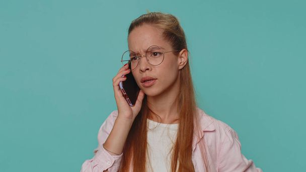 Tired teenager student girl making online conversation speaks on smartphone. Boring call. Blah expression. Nonsense talk. Young stylish teen female child kid isolated alone on blue studio background - Foto, imagen