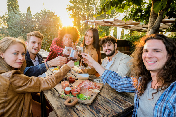 Ομάδα πολυεθνικών φίλων που ζουν υγιεινό τρόπο ζωής και χαμογελώντας και αστειεύεται, ενώ κάνει απεριτίφ και πίνοντας κόκκινο κρασί σε υπαίθριο εστιατόριο παμπ - Φωτογραφία, εικόνα