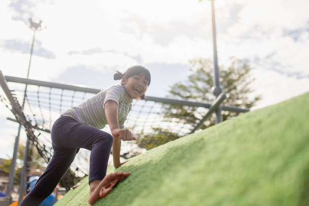Cute Asian girl having fun trying to climb on artificial boulders at schoolyard playground, Little girl climbing up the rock wall, Hand Eye Coordination, Skills development - 写真・画像