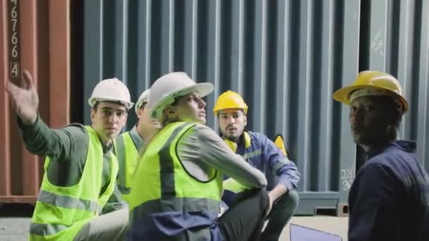 Group of multiracial workers in safety uniforms and hardhats sit and discuss logistics with White male manager, trading shipping goods for cargo transportation industry, shot from inside a container.  - Video, Çekim